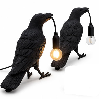 Black raven table lamp glowing warmly on a wooden bedside table